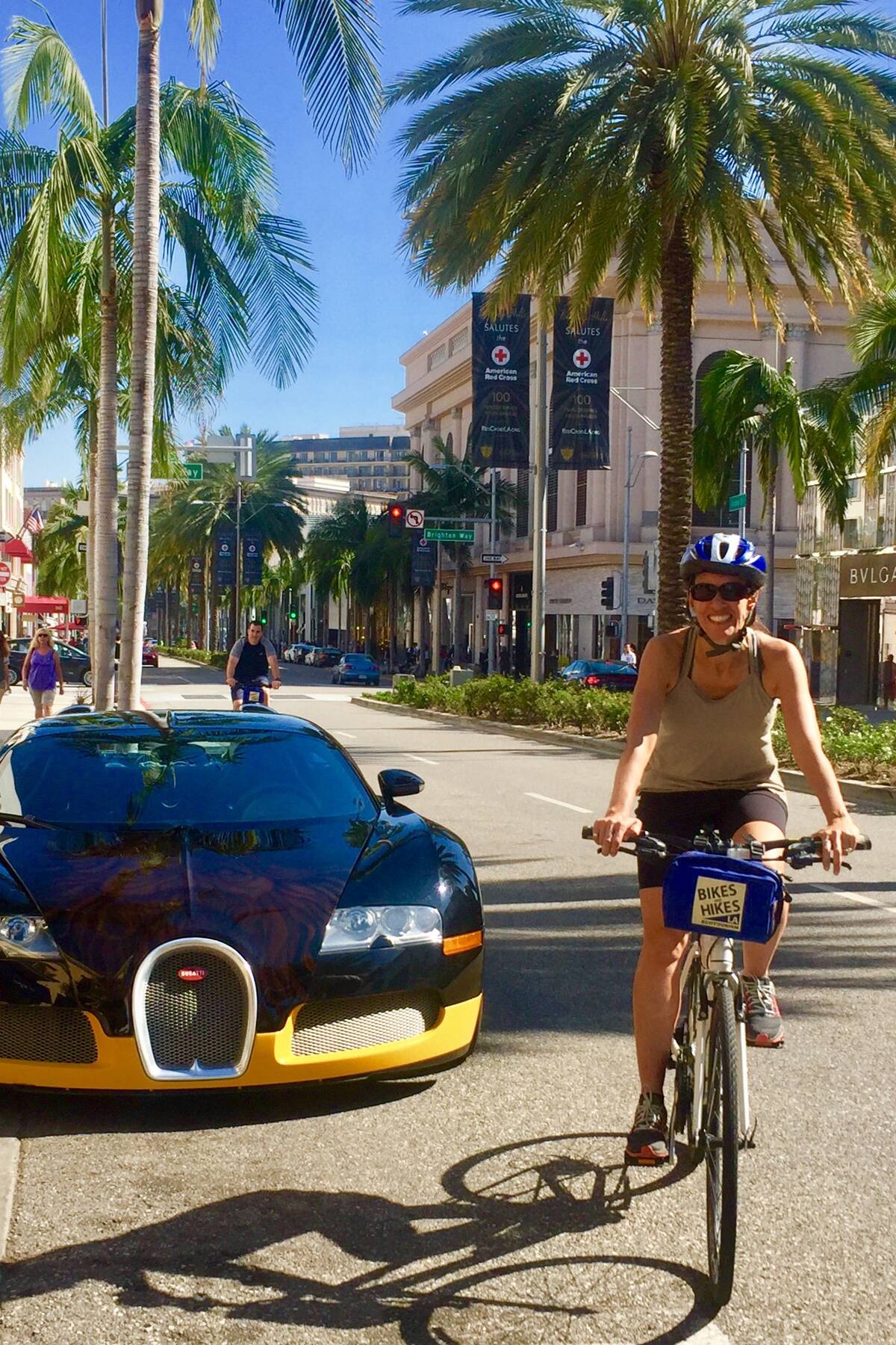 A guest poses with her bike on the Beverly Hills Tour next to a Yellow and Black Rolls Royce