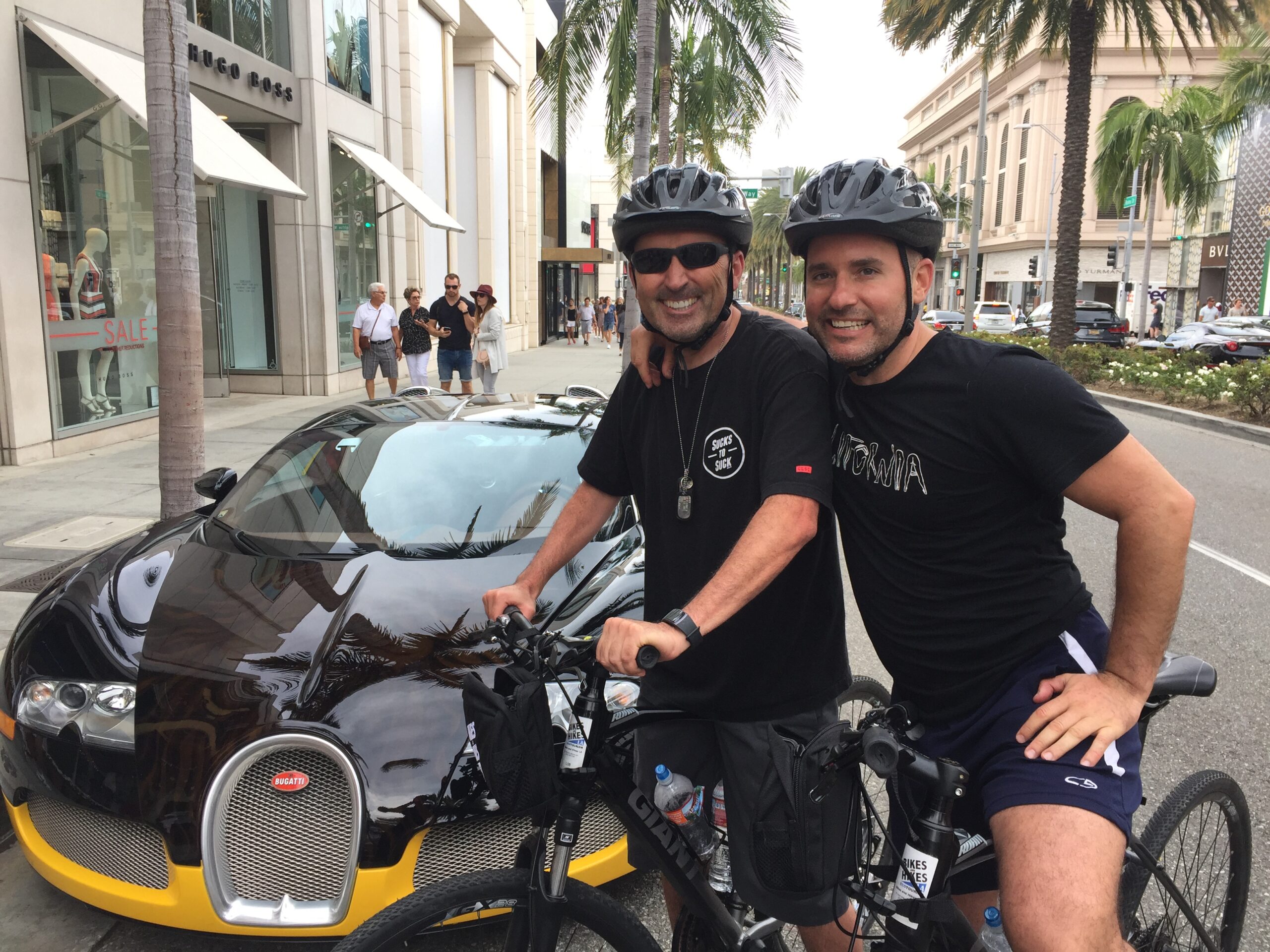 Two men pose in front of a fancy car on Rodeo drive on the Beverly Hills Tour