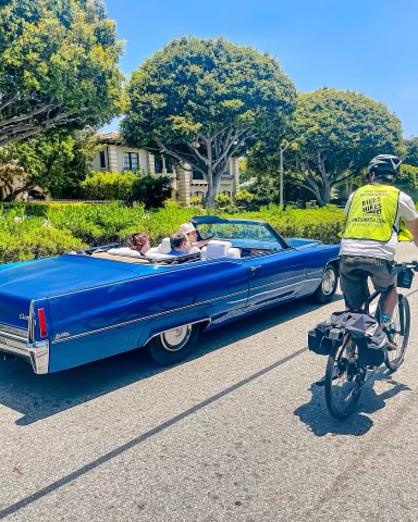A guest rides past a fancy car on the Beverly Hills Tour