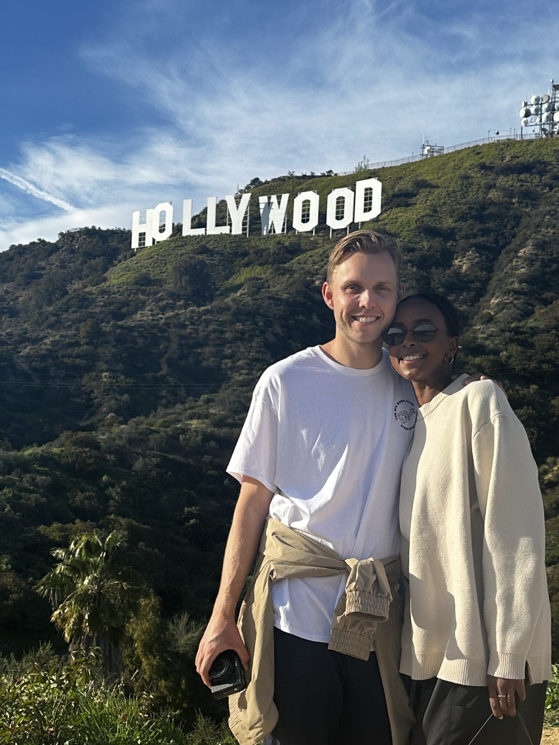 A cute couple poses in front of the Hollywood Sign on the Hollywood Sign Tour