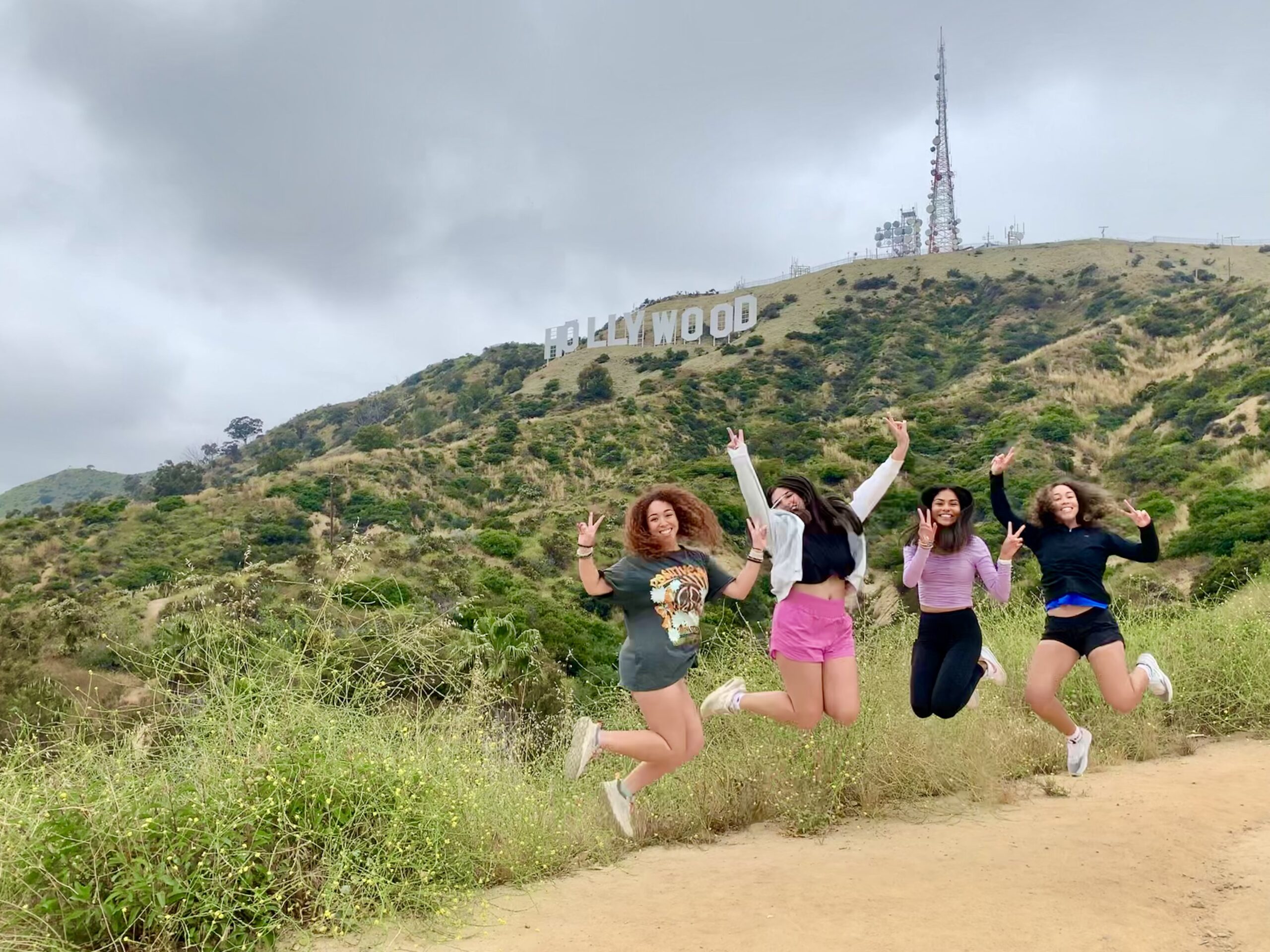 Girls jump in the air and pose underneath the Hollywood sign on the Hollywood Sign Tour