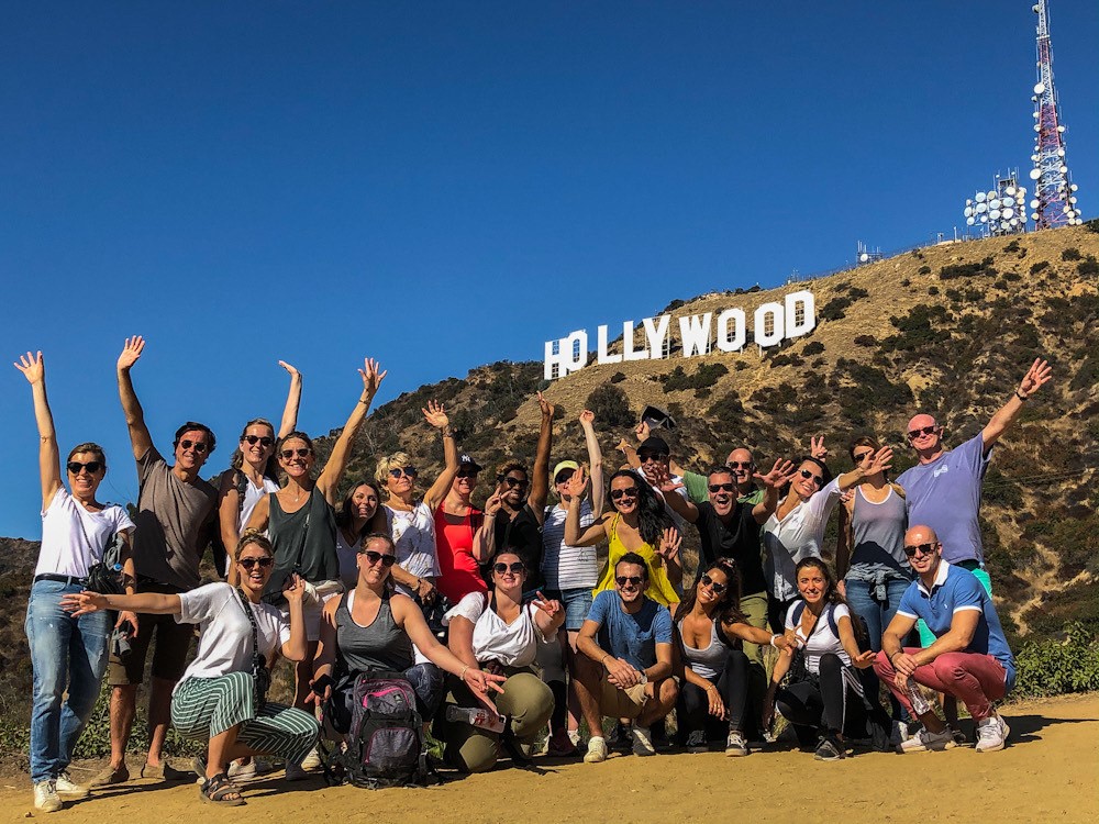 A large group of people pose in front of the Hollywood Sign on the best Hollywood Sign Tour